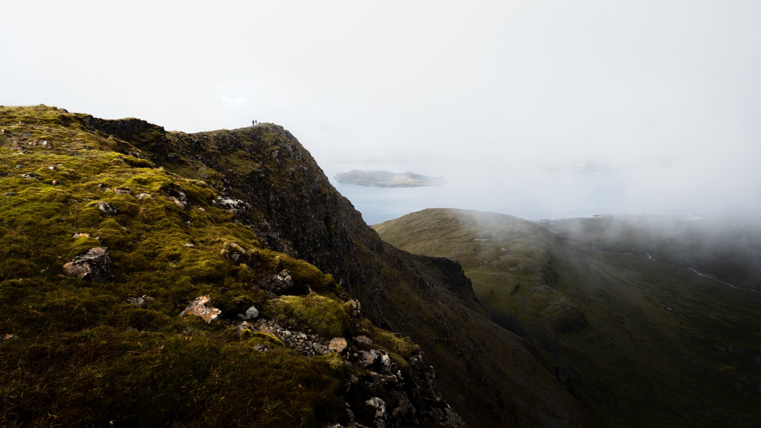 Figure on top of rocks overlooking lake and snowy mountains. 