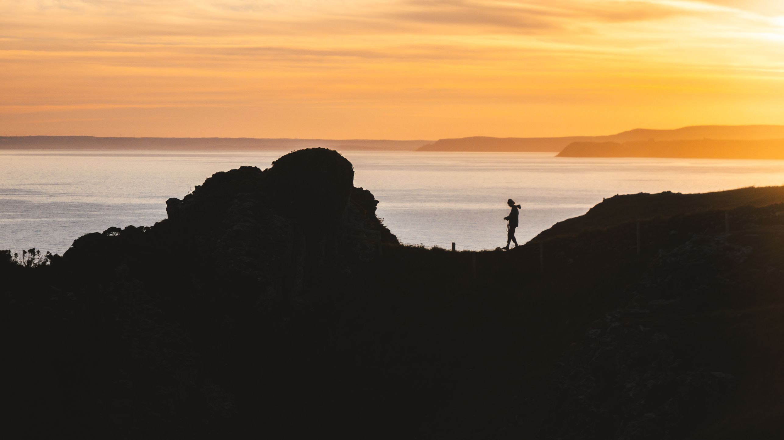 Figure walking along ridge looking over ocean 