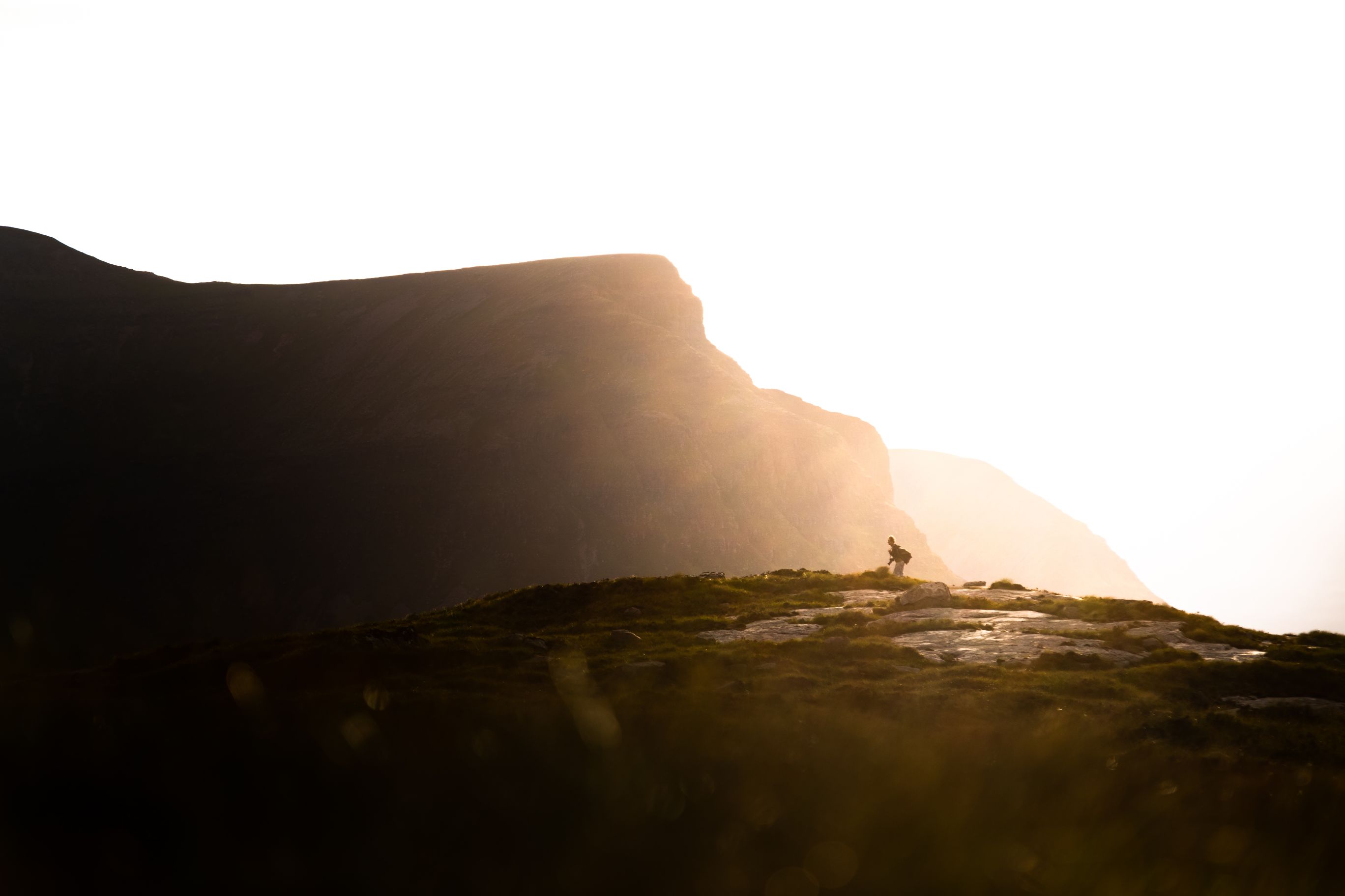 Man walking across rocks with a mountain in the background. 