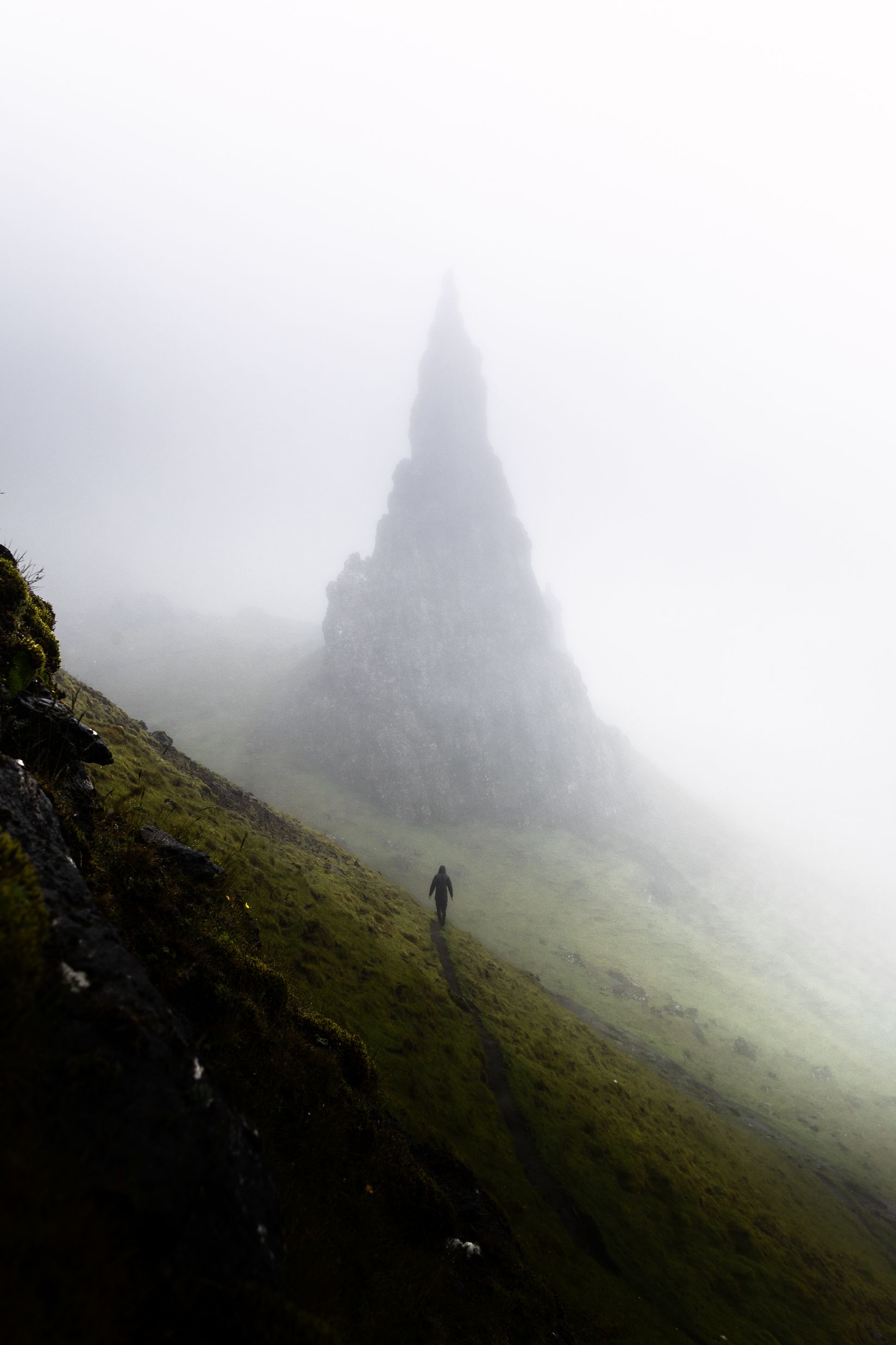 A figure walking in the mist towards rocky peak. 