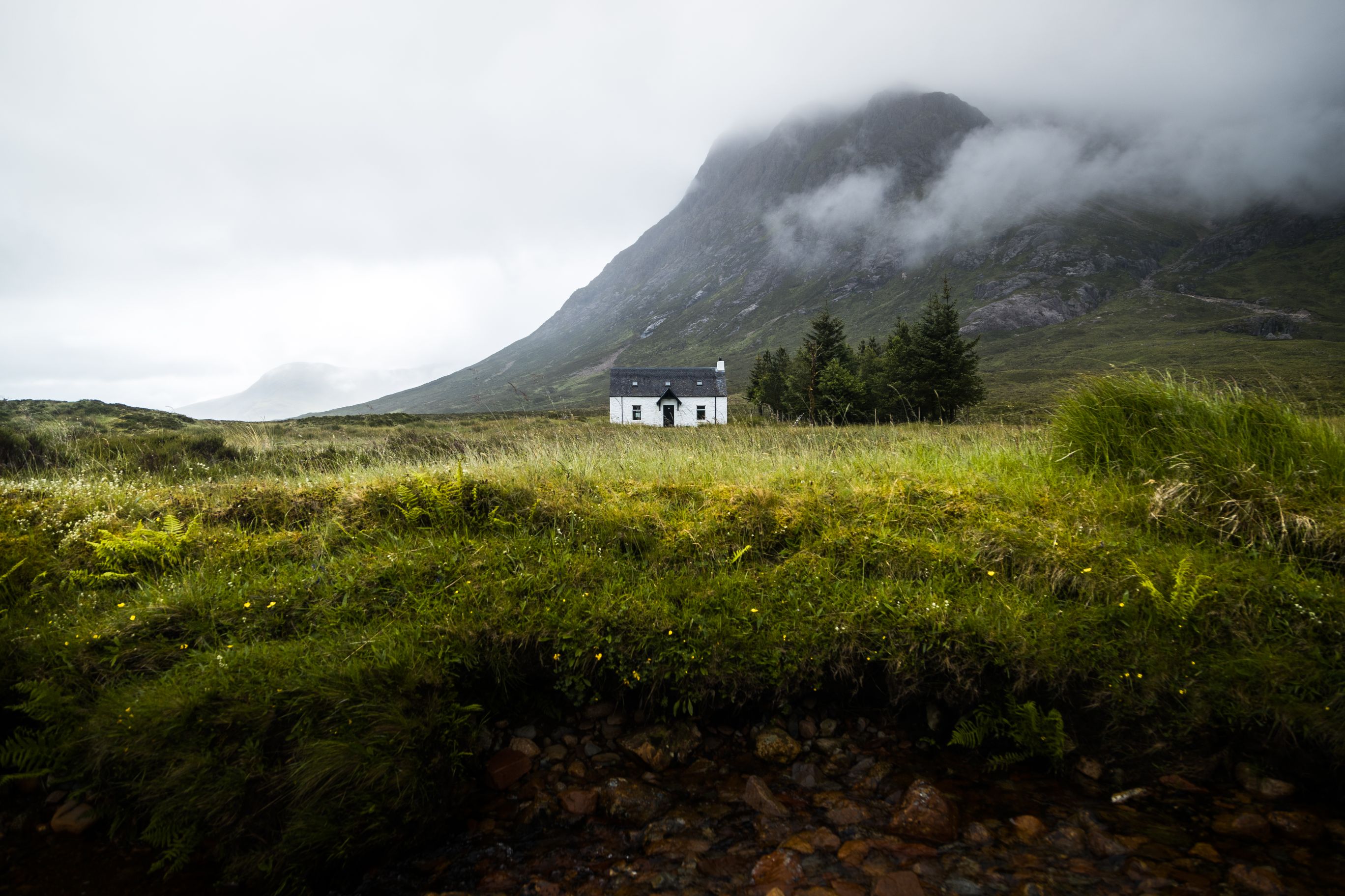 A lone house set amongst grassy field and mountain. 