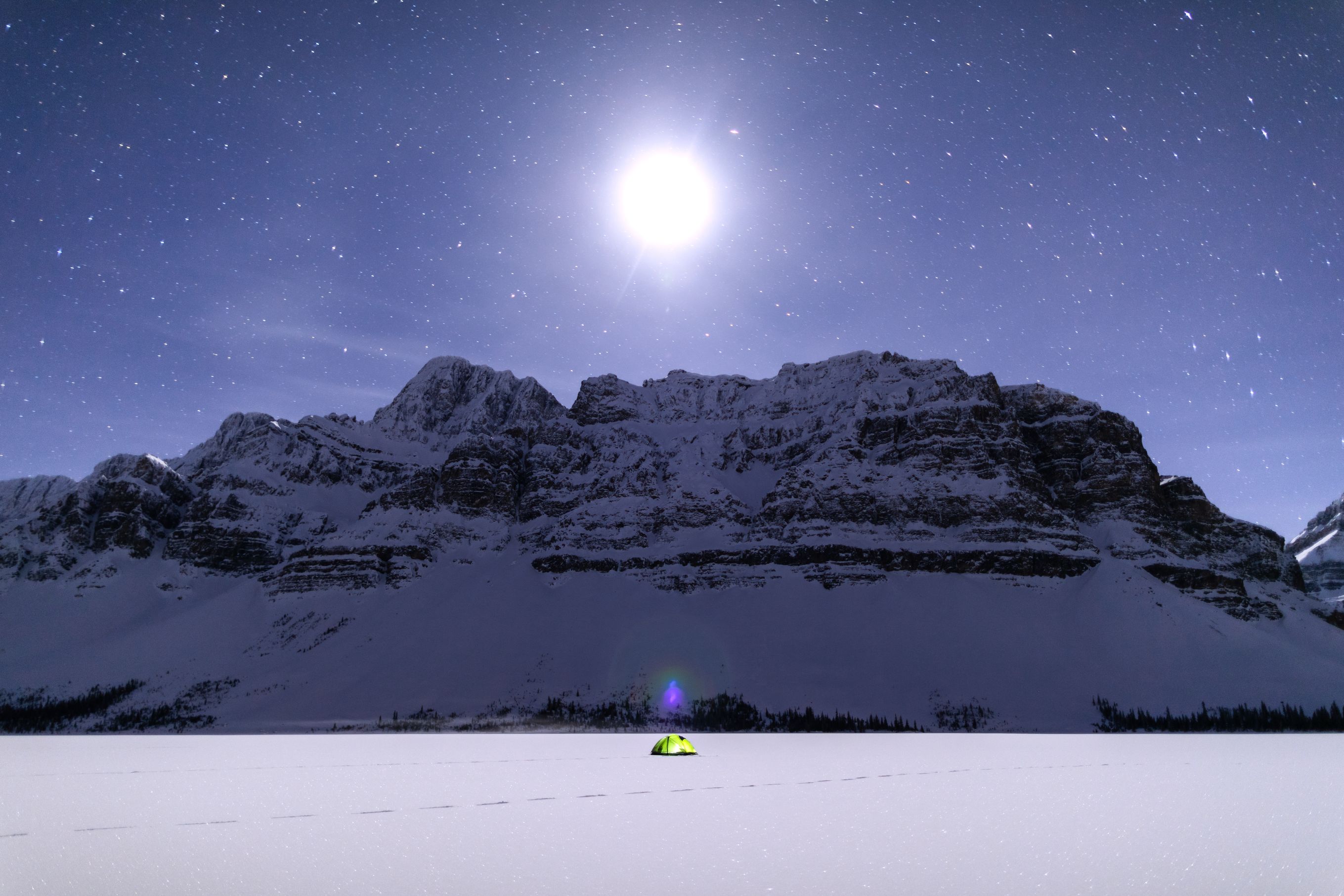 Single tent on a frozen lake in front of rocky mountain. 