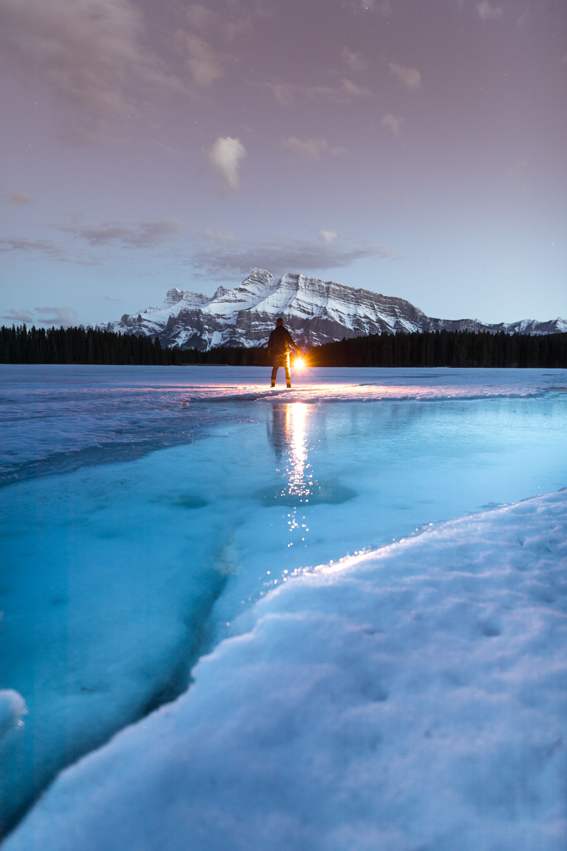 A man standing on a half frozen lake holding a lamp.